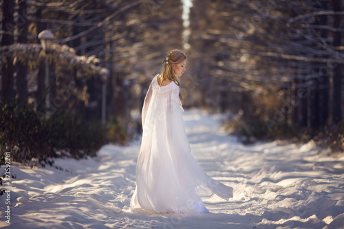 Beautiful girl in a white dress walks in the winter forest. Bride on a background of a winter landscape