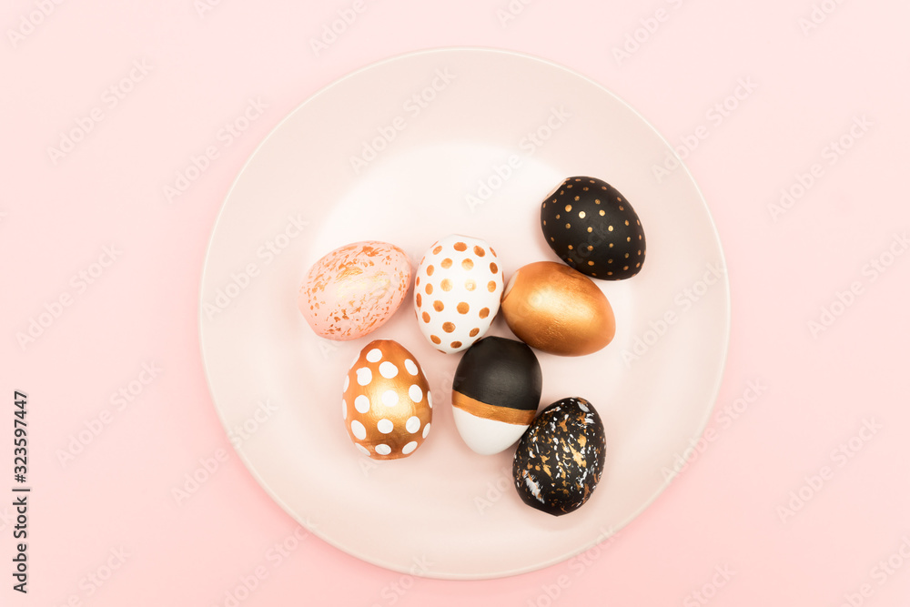 Top view of pink, white and golden decorated eeaster eggs on pink plate on pink background. Trendy holiday backdrop.