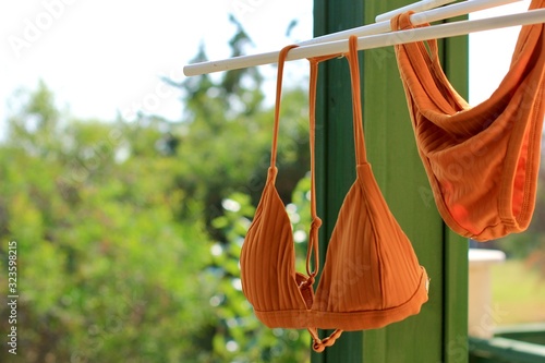 Bright orange bikini swimsuit hanging air drying on clothing line on balcony. Summer concept of vacation, relax, holiday.