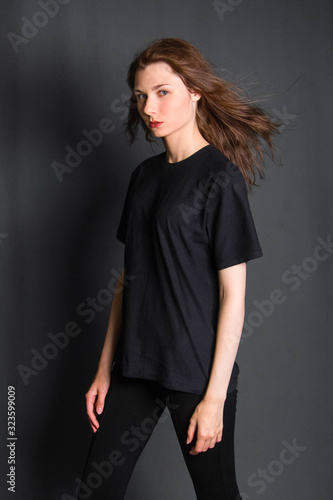 Beautiful, young girl with long hair, in black clothes, posing in studio on a gray background. A model with clean skin.