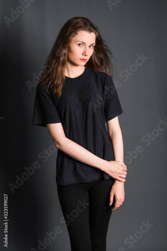 Beautiful, young girl with long hair, in black clothes, posing in studio on a gray background. A model with clean skin.