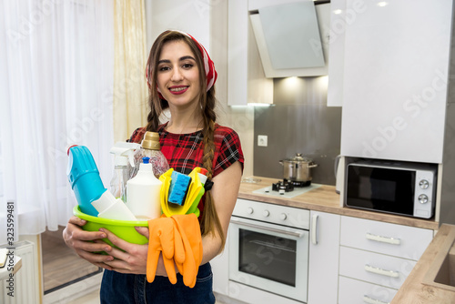 Smiling adult girl cleaning kitchen with spray bottle and a microfiber cloth.