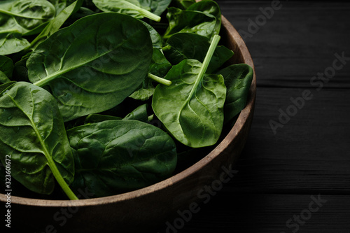 wooden plate with fresh spinach leaves on black background. closeup