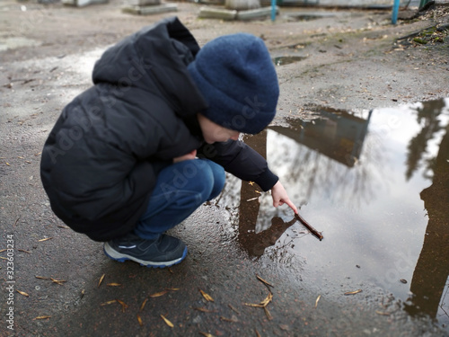 little boy plays in a puddle on an autumn day