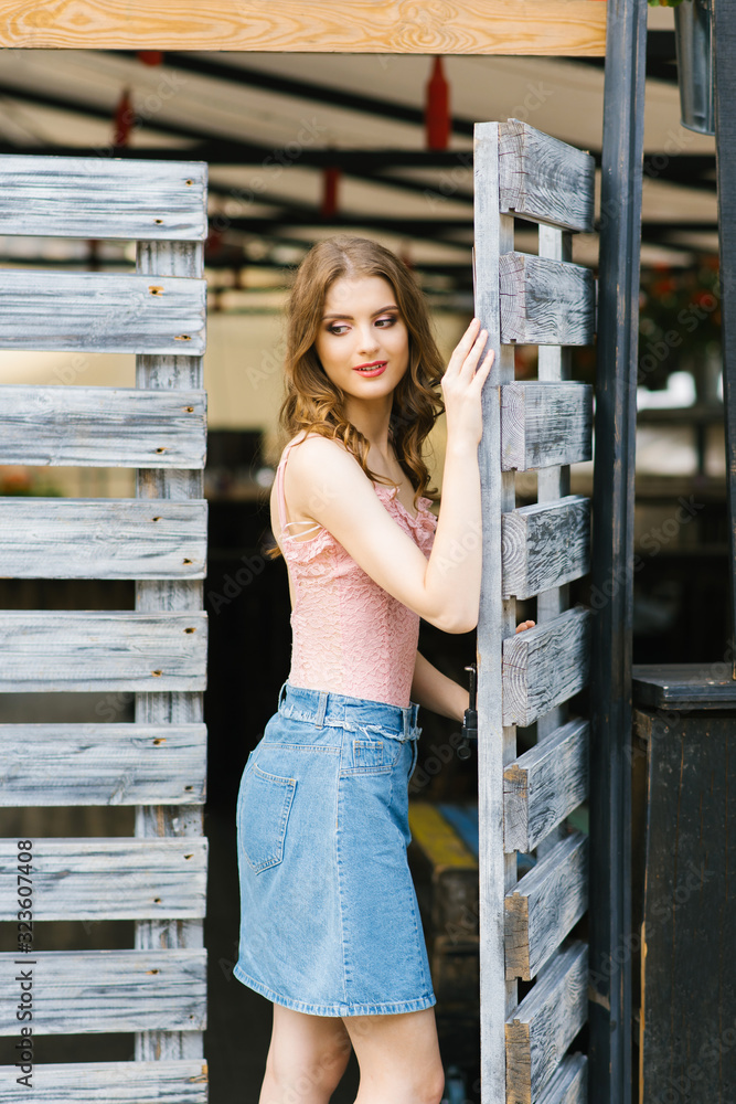 A beautiful young Caucasian girl stands near a wooden gate A beautiful young Caucasian girl stands near a wooden gate