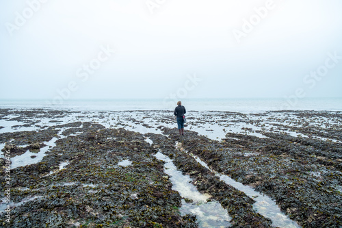Woman wearing warm clothes and a purse looking out over a foggy sea from a pebble beach on the shore