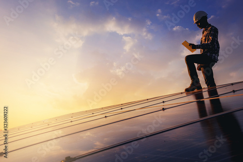 Electrical, instrument technician use touch pad manual guide to maintenance electric system and standing relax on the solar panel with sunset sky