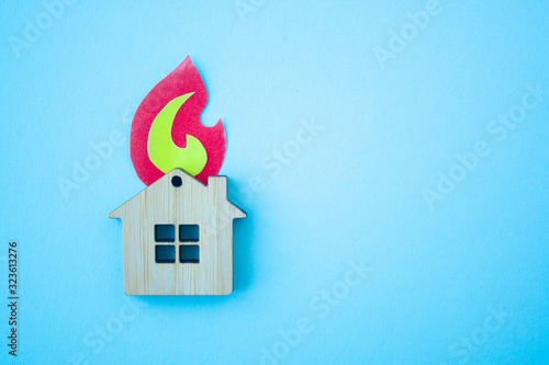 Fire house, insurance and mortgage concept. Small wooden house toy and paper fire shape on blue background top view with copy space