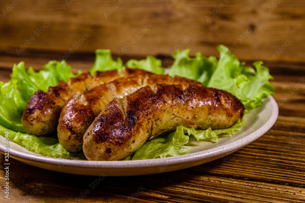 Plate with roasted sausages and lettuce leaves on a wooden table