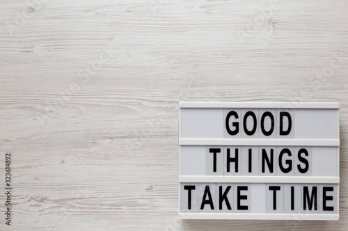'Good things take time' words on a modern board on a white wooden background, top view. Overhead, from above, flat lay. Copy space.
