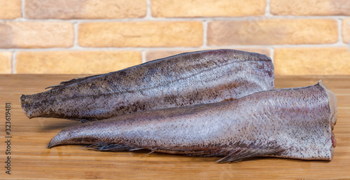 Uncooked defreezed carcasses of hake on wooden surface close-up photo