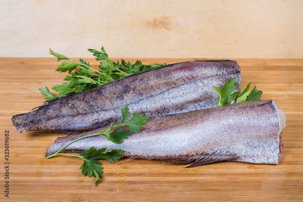 Uncooked defreezed hake carcasses among parsley on the wooden surface Uncooked defreezed hake carcasses among parsley on the wooden surface