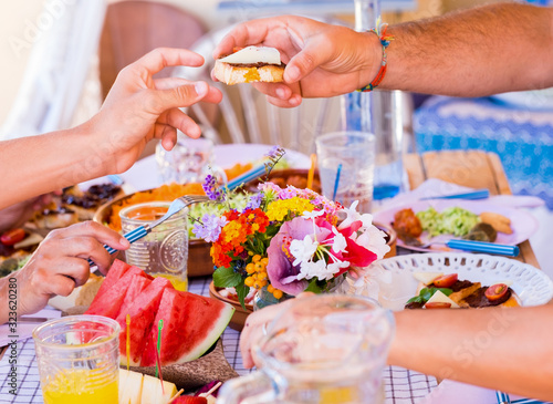 Group of hands sharing food and drink. Caucasian peoples enjoying brunch or meal together. Fruits and vegetables on the wooden table. Sunlight outdoor on the terrace
