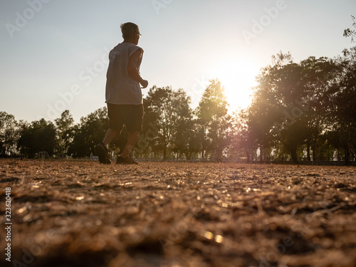 Asian senior man jogging in the park over sunset sky background. Healthy lifestyle and Healthcare concept. © scentrio