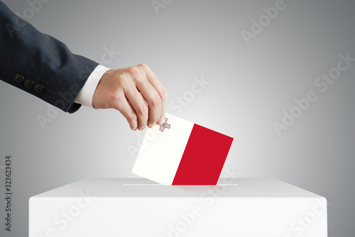 Man putting a voting ballot into a box with Maltese flag.