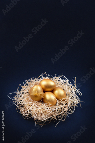 Golden colored Easter eggs in decorative nest on dark blue background. Happy Easter greeting card. Easter background. Place for text.