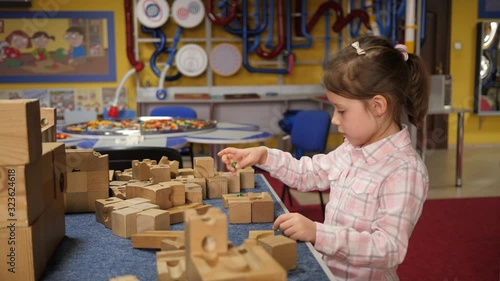 Little kid girl play wooden constructor assembles details of mind charging puzzle in playground room photo