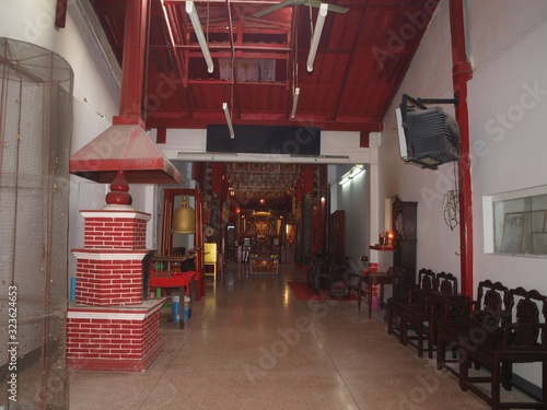 Entrance to the buddhist temple. Chinatown. Small temple in the house. View from an enter. Corridor, chairs along a wall, golden Buddha statues, offering table in a far, brick furnace for ritual fire.