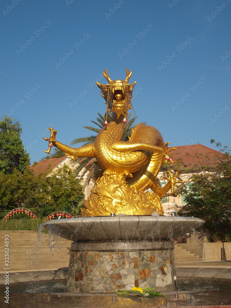 Golden sea dragon fountain and sculpture in a asian city park. Front view in the rays of the setting sun. Water flows at the bottom of the monument, like waters of the ocean from which dragon appears
