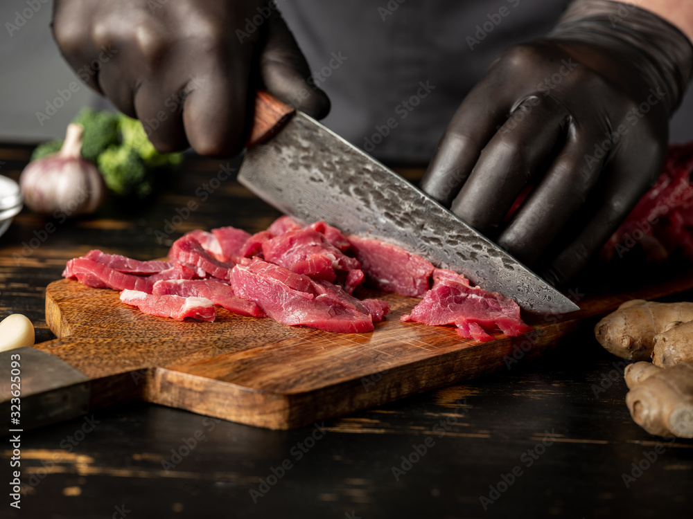 Chef cutting raw selected meat on wooden desk with big knife. Cooking recipe concept.