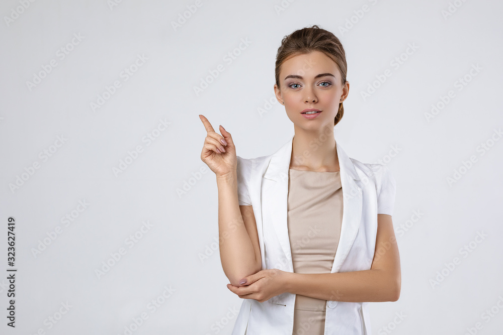 smiling young beautiful business woman in white jacket pointing up and looking at the camera on gray background. copy space smiling young beautiful business woman in white jacket pointing up and looking at the camera on gray background. copy space