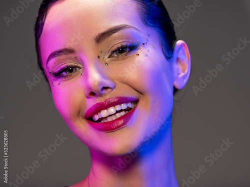 Portrait of happy girl. Laughing face of a beautiful model. Colorful portrait of a girl with bright makeup. Shiny sequins on the face. Art portrait. Happy woman. Young positive girl in a bright image.