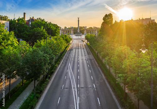 Budapest, Hungary - Aerial drone view of totally empty Andrassy street at sunrise with green trees and sunlight and Heroes' Square (Hosok tere) at background at summer time photo