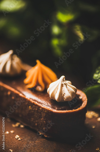 Contemporary dessert. Belgian chocolate, Swiss merenge and caramel tart over rusty dark background, close-up, selective focus. Cafe or modern patisserie concept photo