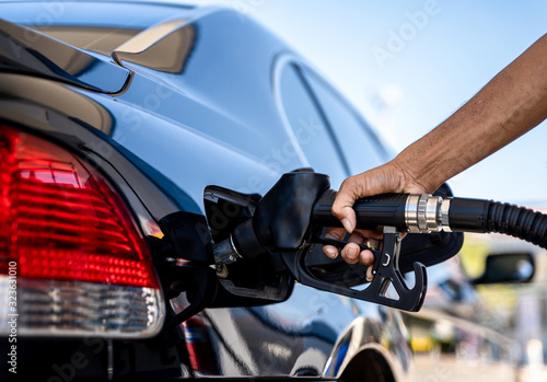 Hand holding fuel pump and refilling car at petrol station. © Chinnabuth