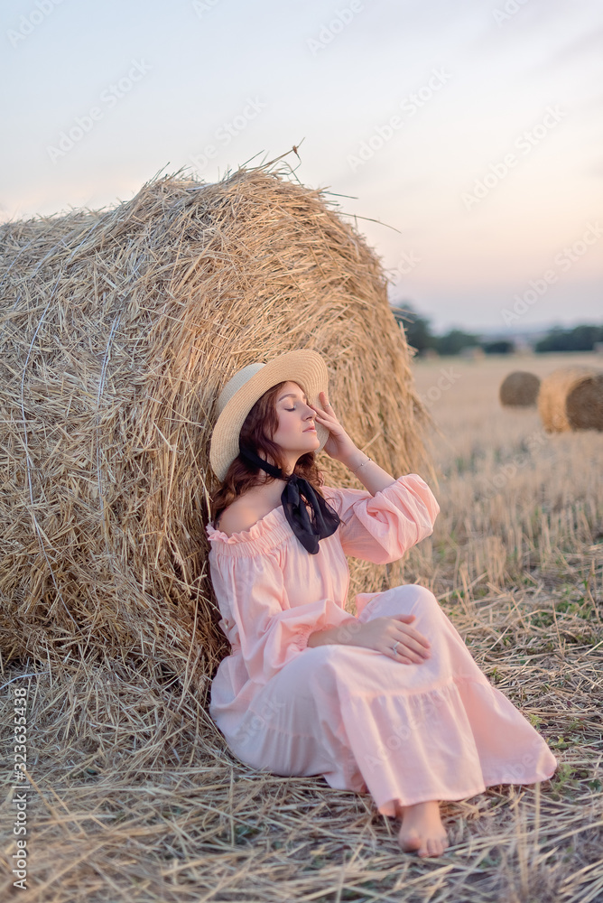 Attractive girl in dress sitting on sheaves of hay Attractive girl in dress sitting on sheaves of hay