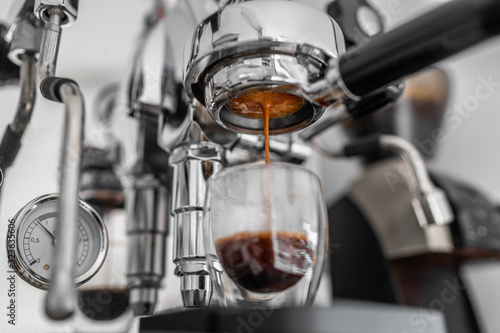 Coffee machine pouring single shot espresso in double wall glass from bottomless naked portafilter. Professional equipment at home or cafe. © Maridav