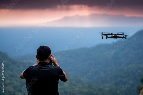 Man operating drone flying or hovering by remote control in the jungle.