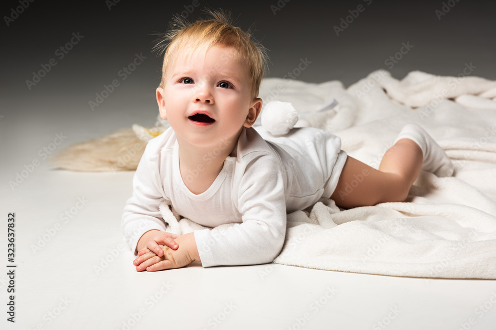 Child with pompon on underpants, lying on blanket, looking up with open mouth on grey background Child with pompon on underpants, lying on blanket, looking up with open mouth on grey background