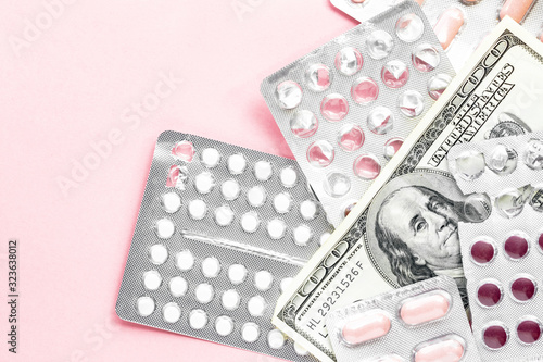 white and pink pills in aluminum blister with one hundred dollar bill on a light pink background, expensive medicine flat lay with copy space