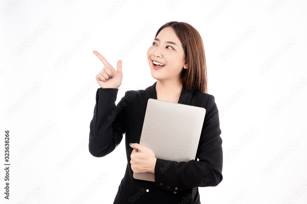 Asian businesswoman with black suit holding a laptop and pointing to present copy space with big smile beaming face in white isolated background. Asian businesswoman with black suit holding a laptop and pointing to present copy space with big smile beaming face in white isolated background.