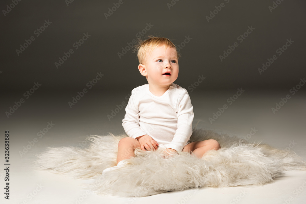 Cute child looking away with open mouth, sitting on fur on black background Cute child looking away with open mouth, sitting on fur on black background