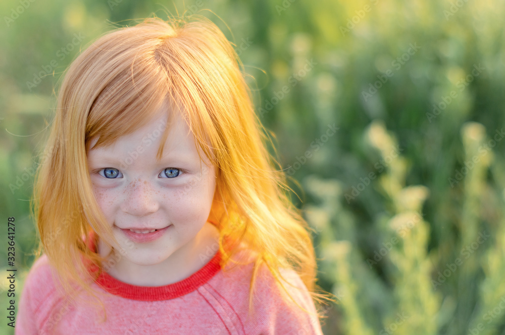 Beautigful little girl with blue eyes and red hair smiling on a background of green grass Beautigful little girl with blue eyes and red hair smiling on a background of green grass