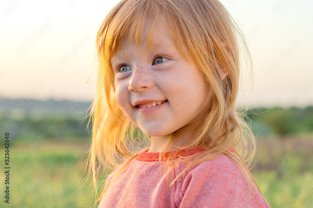 Beautigful little girl with blue eyes and red hair smiling on a background of green grass Beautigful little girl with blue eyes and red hair smiling on a background of green grass