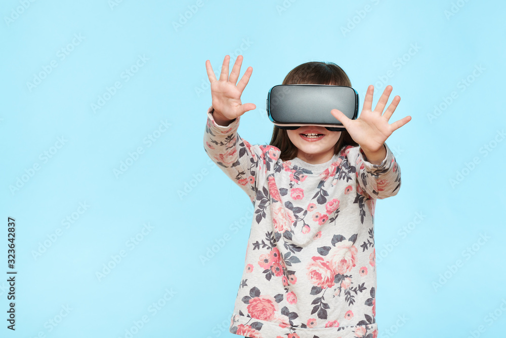 Studio portrait of cute young caucasian girl wearing virtual reality glasses against pastel blue background. Future gadgets technology concept. Studio portrait of cute young caucasian girl wearing virtual reality glasses against pastel blue background. Future gadgets technology concept.