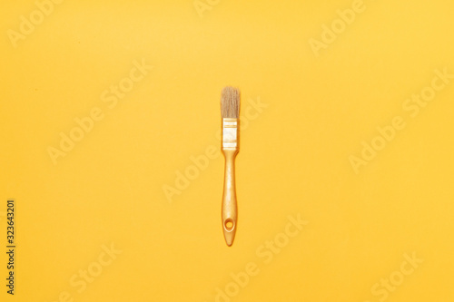 Gold paint brush on a yellow background. Minimal composition