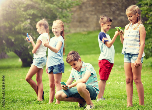 childhood, augmented reality, internet addiction, technology and people concept - group of kids or friends with smartphones playing game in summer park
