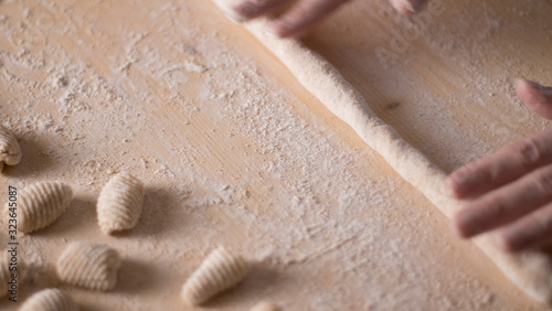 Close up process of homemade vegan gnocchi pasta with wholemeal flour making. The home cook rolls the dough on the wooden chopping board , traditional Italian pasta, woman cooks food in the kitchen