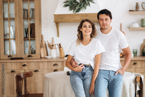 Morning at home. Portrait of a beautiful couple in love in the kitchen. The guy and the girl are stylishly dressed in white t-shirts and jeans © Kateryna