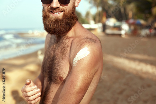 Handsome Man with beard, In Sunglasses Sunbathing With Sunscreen Lotion Body In Summer. Male Fitness Model Tanning Using Solar Block Cream For Healthy Tan. Skincare. Sun Skin Protection © verona_studio