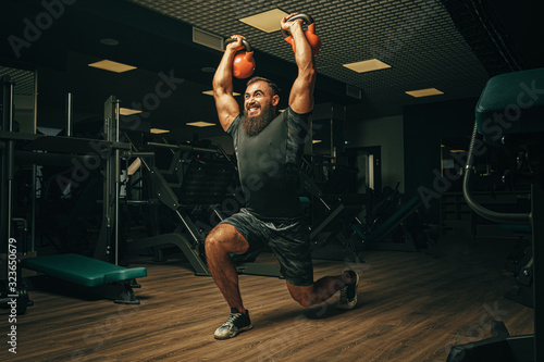 Bodybuilder doing exercises with dumbbells in a dark gym