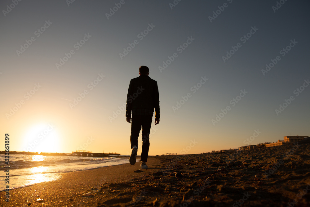 Young man and sunset on Mediteranean sea. One man walking on the beach and looking at the sunset over the sea. Solitary man. A colorful sunset sea, man observing the beauty of nature. 