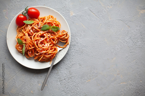 Tasty appetizing classic italian spaghetti pasta with tomato sauce, cheese parmesan and basil on plate on grey backgroound