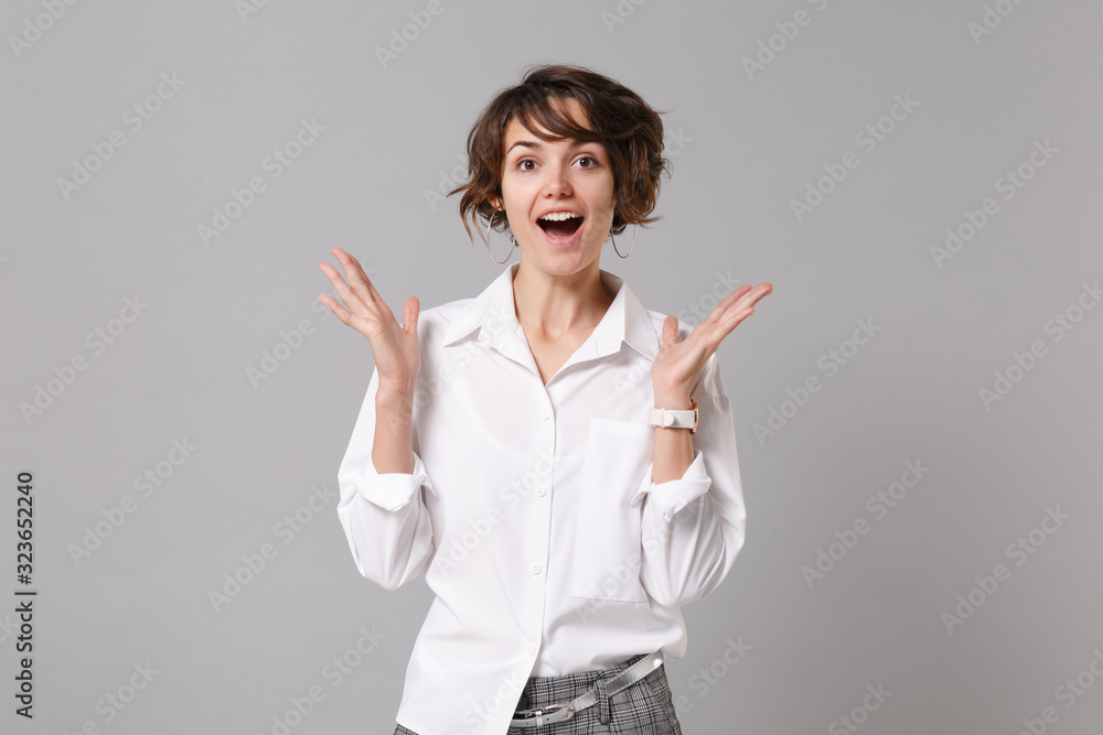 Excited young business woman in white shirt posing isolated on grey background studio portrait. Achievement career wealth business concept. Mock up copy space. Keeping mouth open, spreading hands. Excited young business woman in white shirt posing isolated on grey background studio portrait. Achievement career wealth business concept. Mock up copy space. Keeping mouth open, spreading hands.