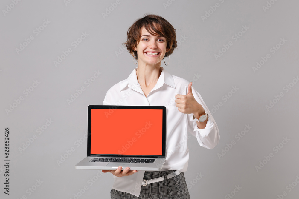 Funny business woman in white shirt posing isolated on grey background. Achievement career wealth business concept. Mock up copy space Hold laptop pc computer with blank empty screen showing thumb up. Funny business woman in white shirt posing isolated on grey background. Achievement career wealth business concept. Mock up copy space Hold laptop pc computer with blank empty screen showing thumb up.