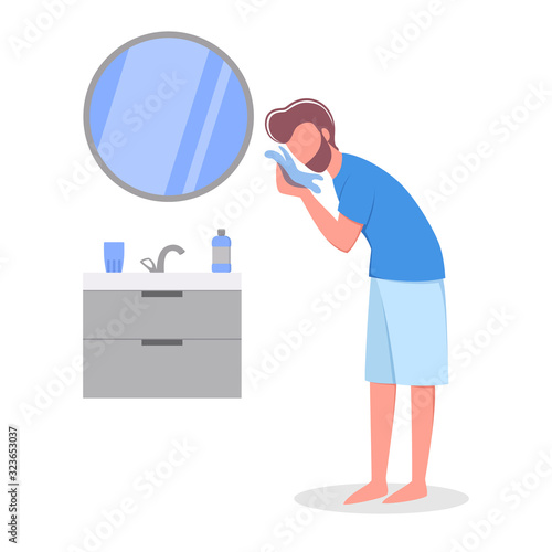 Man standing in the bathroom wiping his face with a towel.
